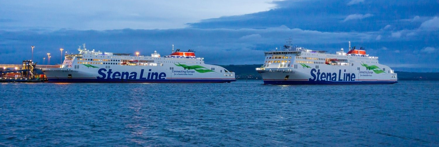 Two Stena Line ferries docked at dusk, with their lights reflecting on the water under a cloudy evening sky.